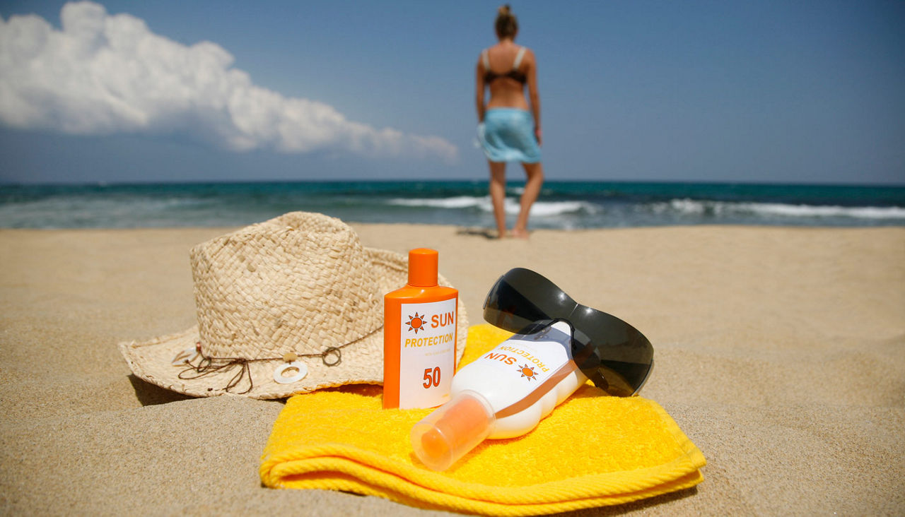 woman on beach with sun protection, sun glasses, beach hat and towel