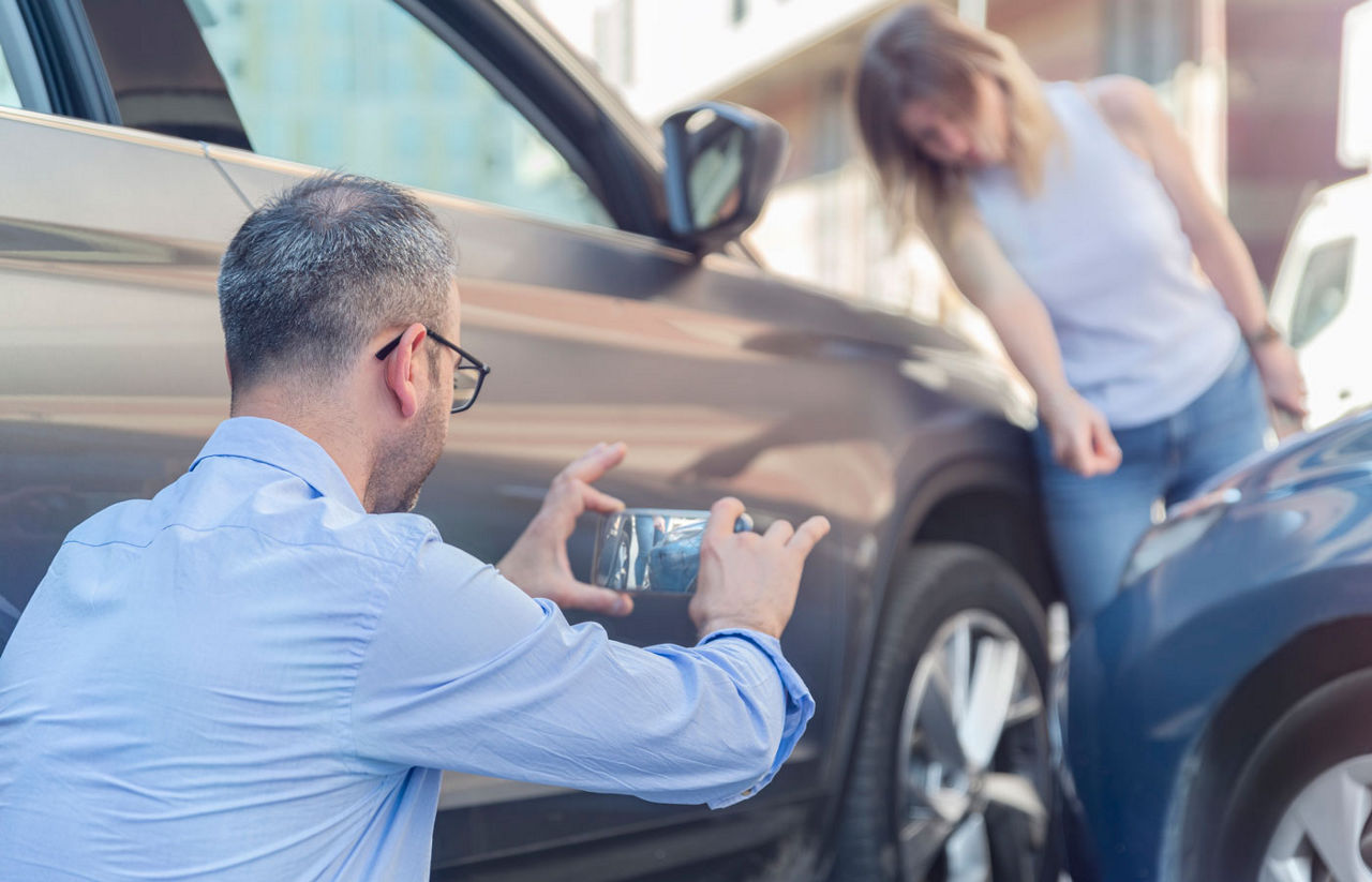 man taking pictures of car damage from accident