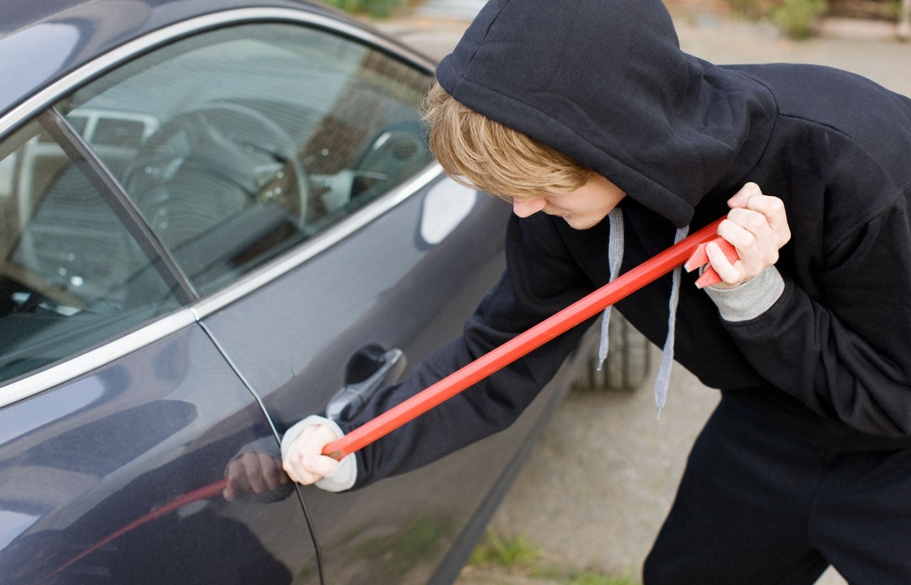 A person pictured prying open a car door in order to steal it.