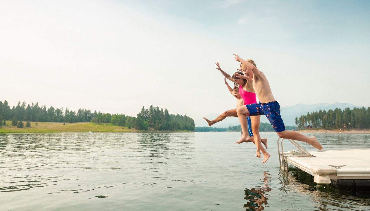 Group of kids jumping off the dock into the lake together during a fun summer vacation.
