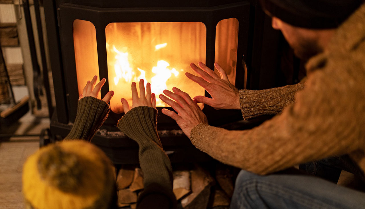 Father and child in warm clothes sitting by indoor fireplace, warming their hands