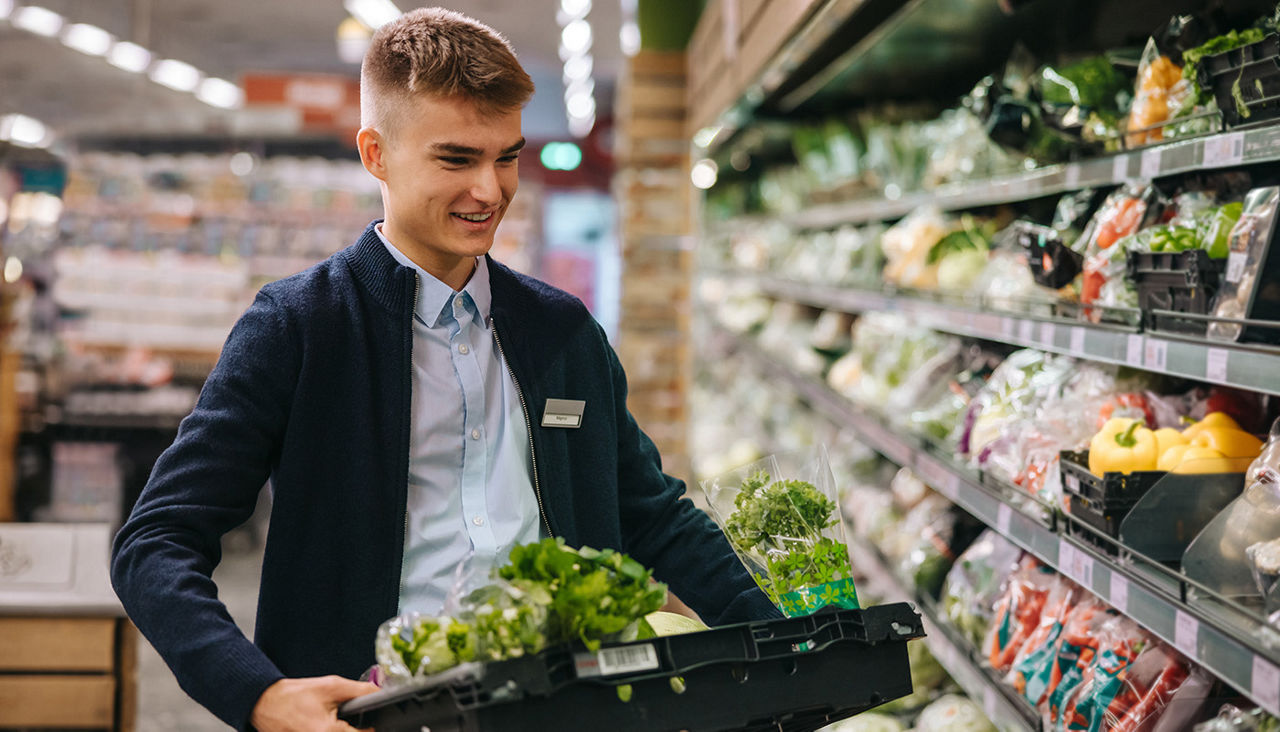 A young min loads fresh vegetables onto displays in produce section of grocery store