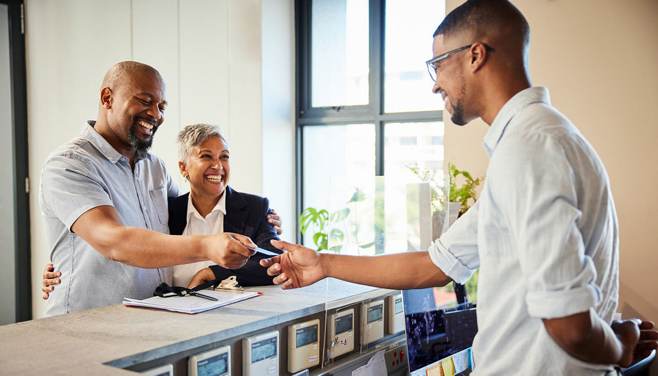 Mature couple handing credit card to hotel employee at reception desk