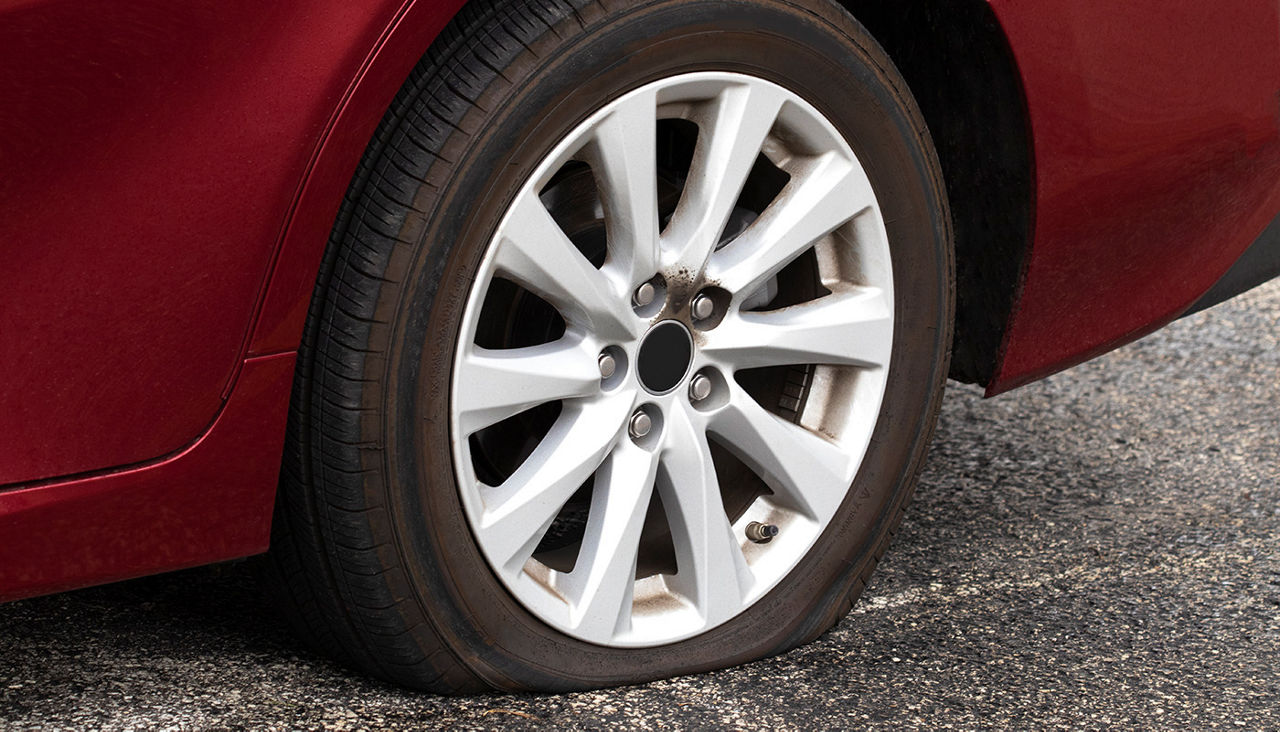 Closeup of flat tire on a red car.