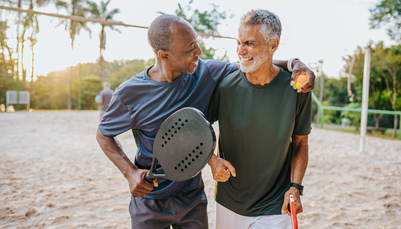 Father and adult son with big smiles walk away from a sand tennis court