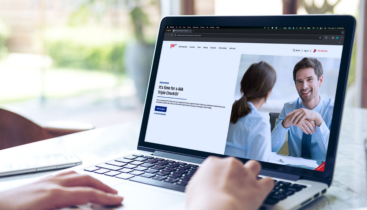 Over-the-shoulder view of a person looking at a laptop displaying a AAA page with insurance information.