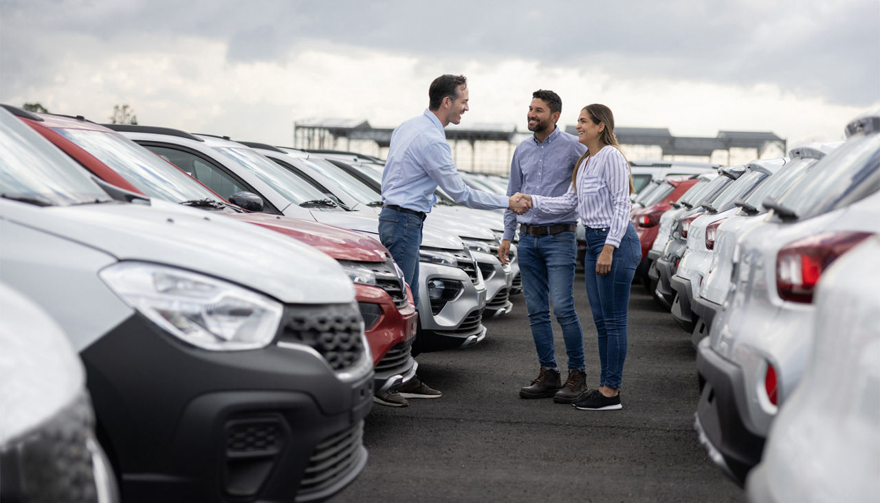 Couple shaking hand with a car salesperson in car lot