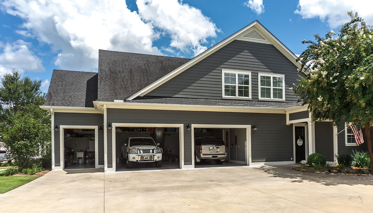 The side view of a large gray craftsman new construction house with a landscaped yard a three car garage and driveway.