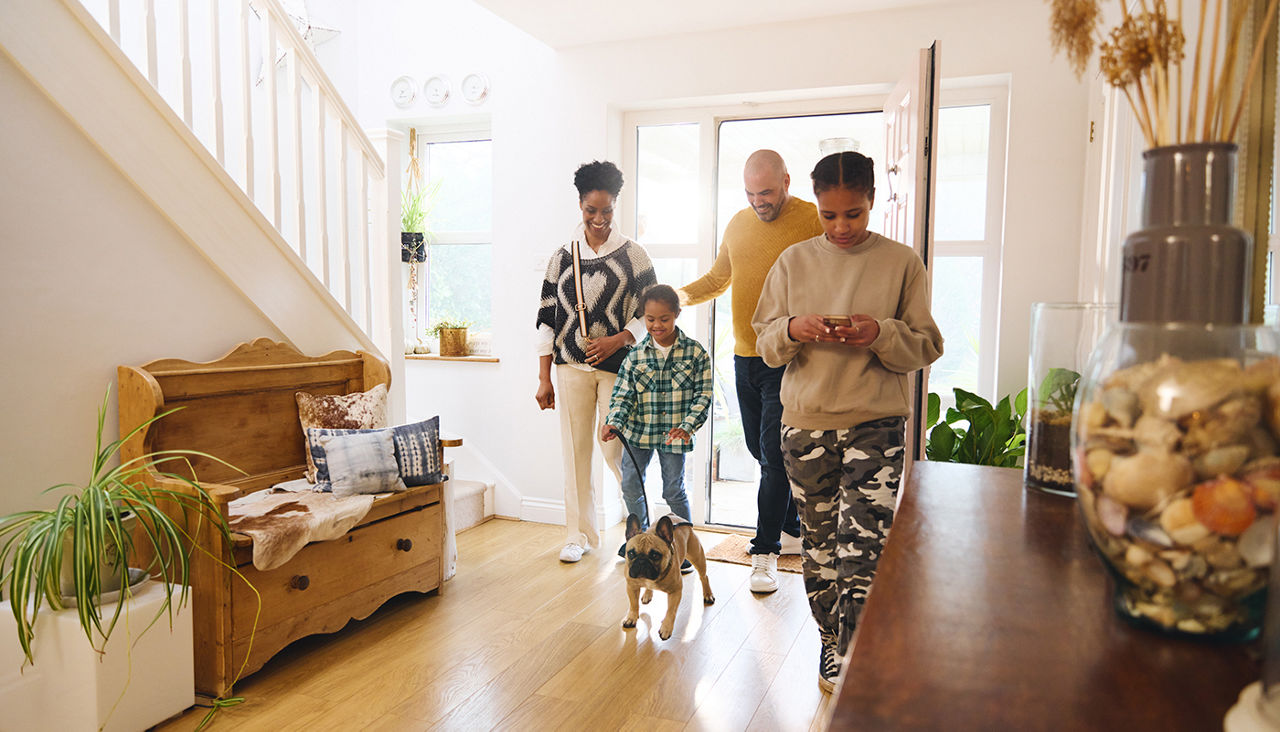 Family arriving home with pet dog, girl using phone