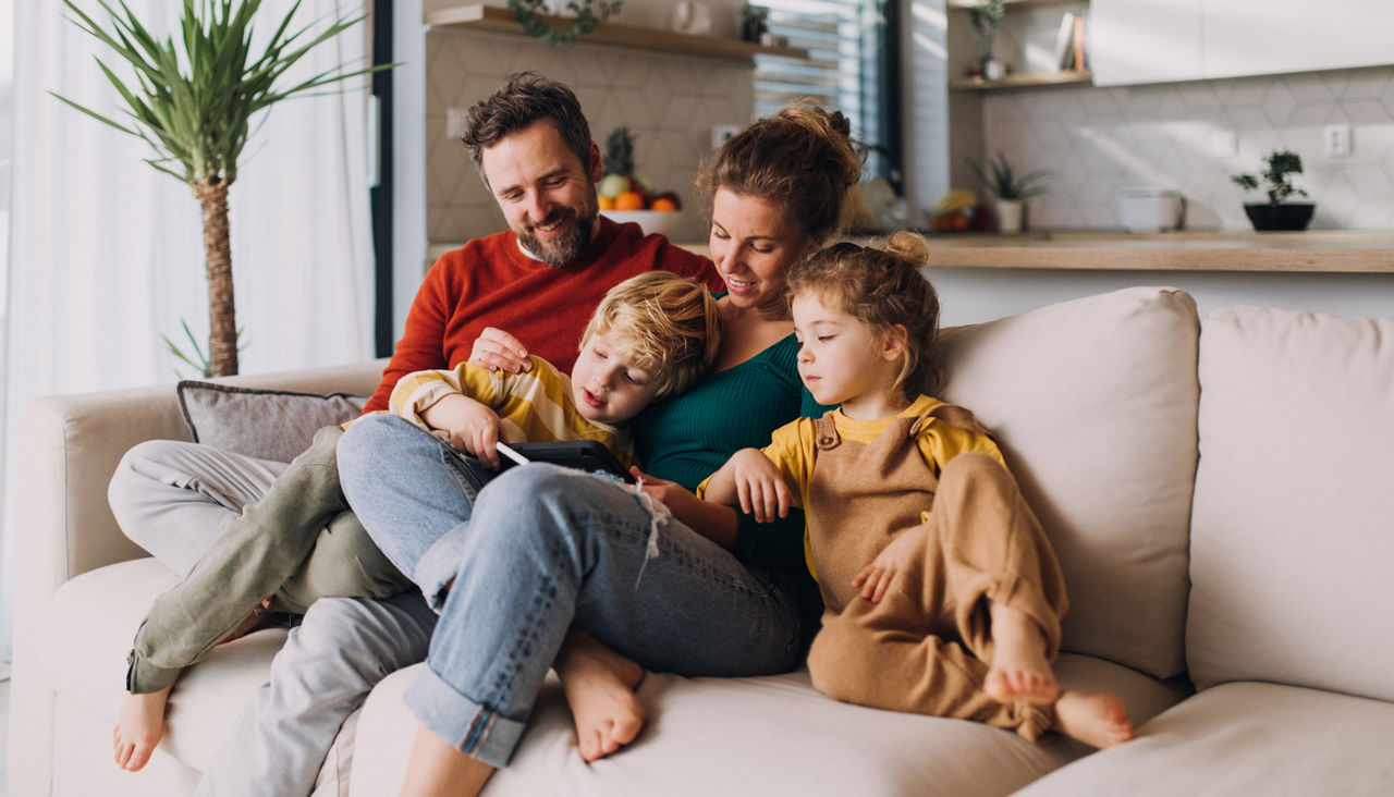 Children bonding with parents on sofa at home and using tablet