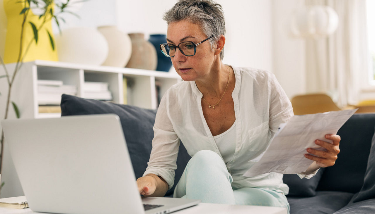 Woman on laptop with documents in hand