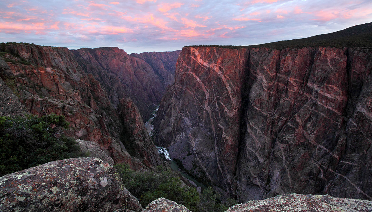 Sun rises over Black Canyon of the Gunnison, Colorado. This cliff is the Painted Wall, the tallest vertical cliff in Colorado, at 2,722 feet. Sunlight barely peeks through the clouds to brighten the top of the cliff with a touch of sunlight.