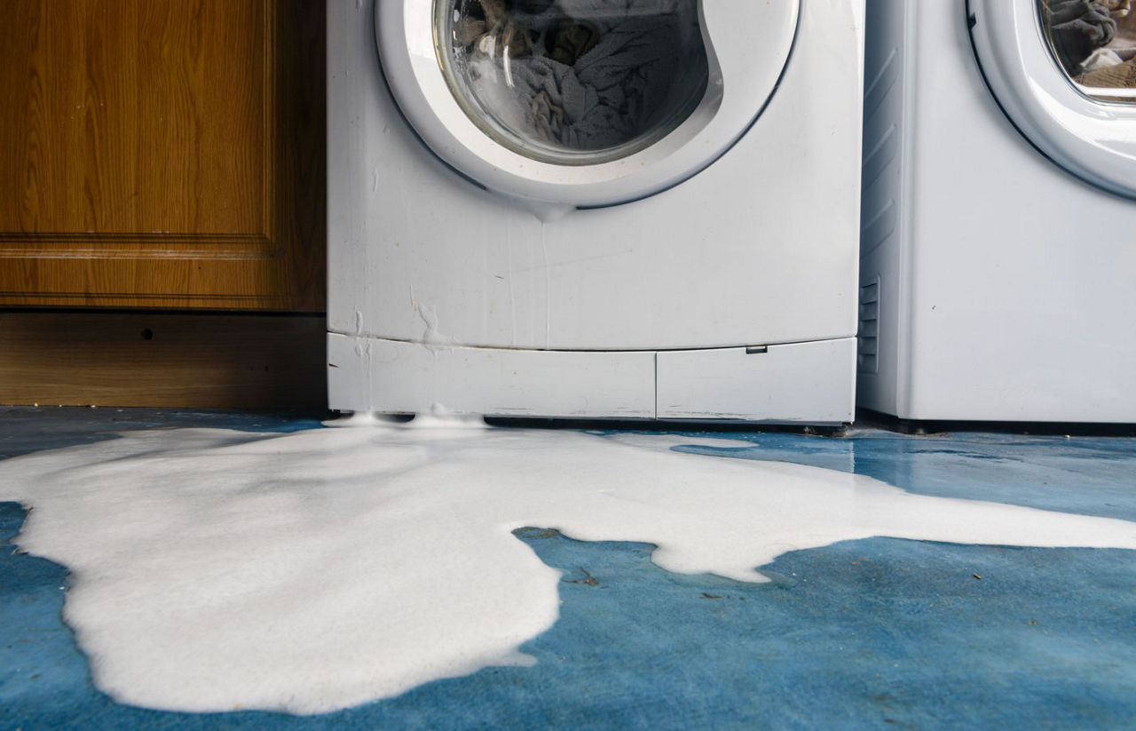 Leaking washing machine with soap suds on the floor in front of it.