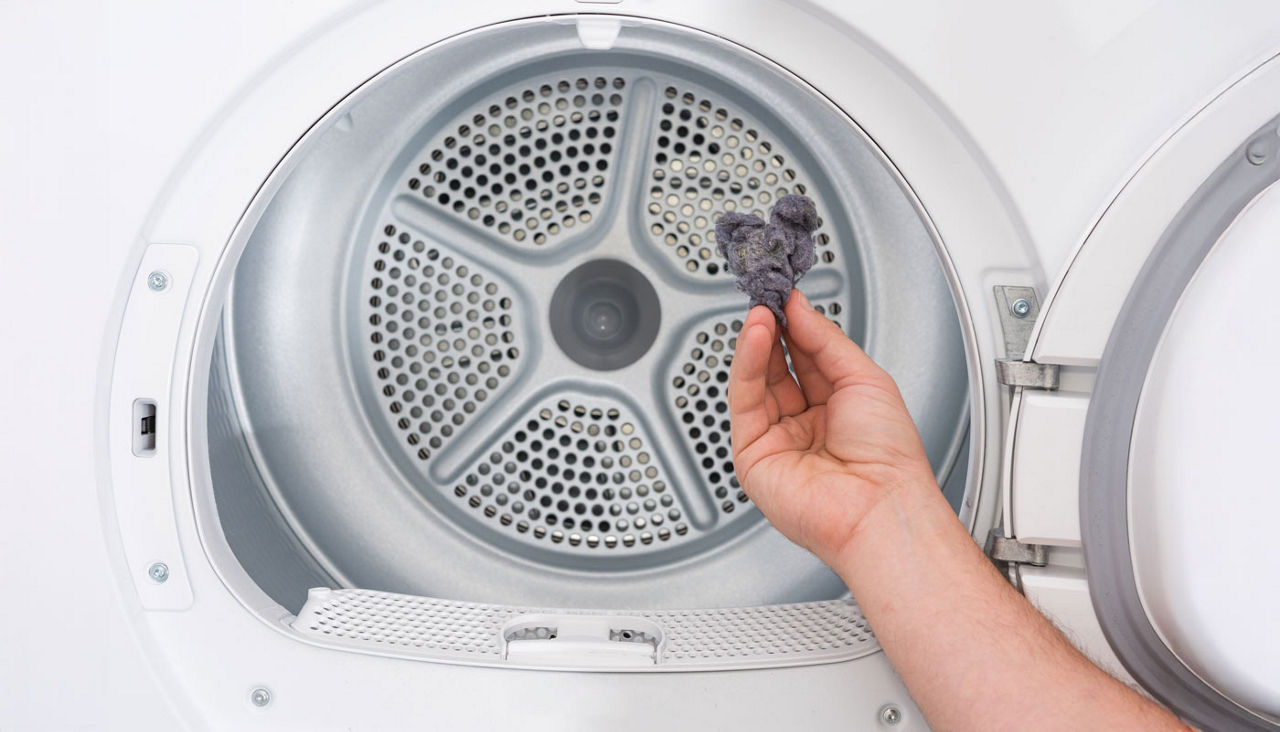 Man's hand holds dust and dirt trapped by clothes dryer filter.