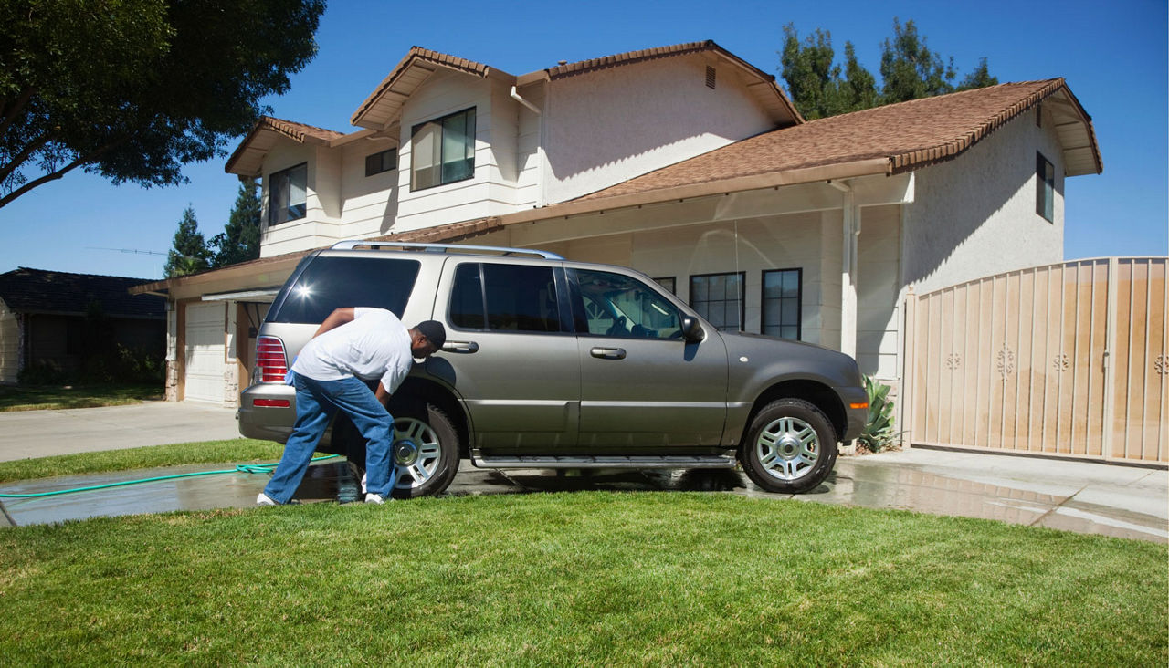man washing his car in front of house