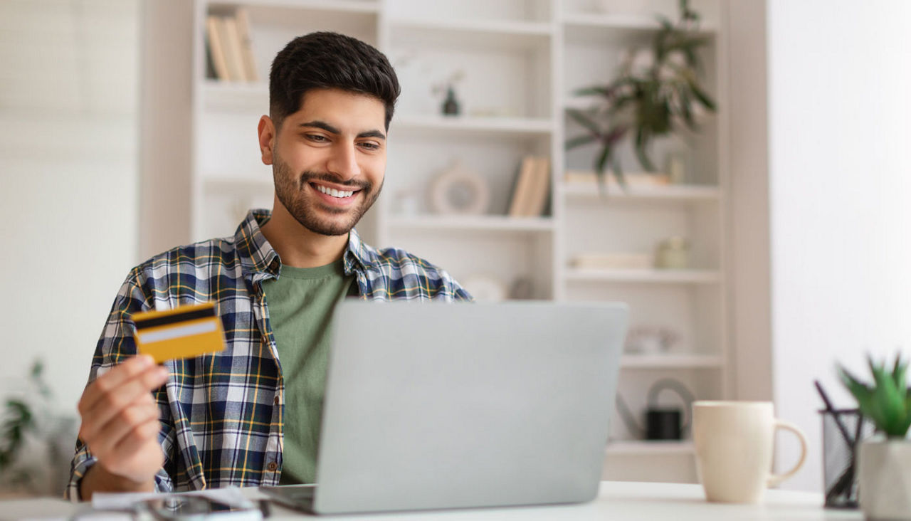 Smiling young man using pc and credit card