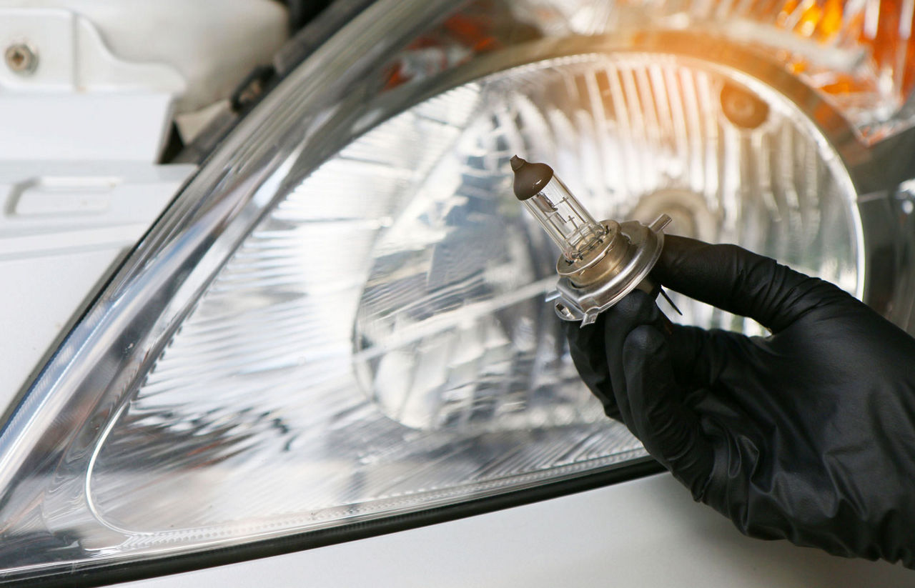 hand holding headlight bulb in front of car headlight