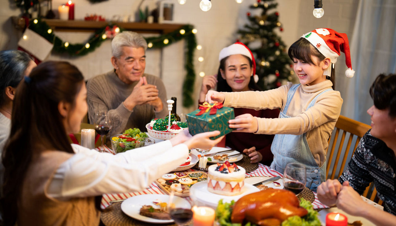 Asian family gathers around the dinner table exchanging gifts celebrating the holiday season together