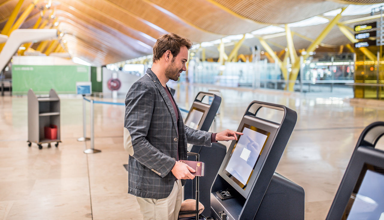 happy man using the check-in machine at the airport getting the boarding pass.