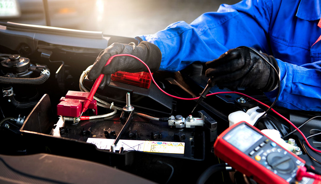 Femal technician uses multimeter voltmeter to check voltage level in car battery. Service and Maintenance car battery.