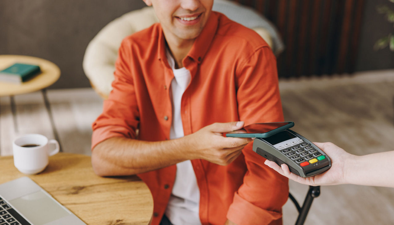 Young man sitting in cafe paying for coffee with his phone