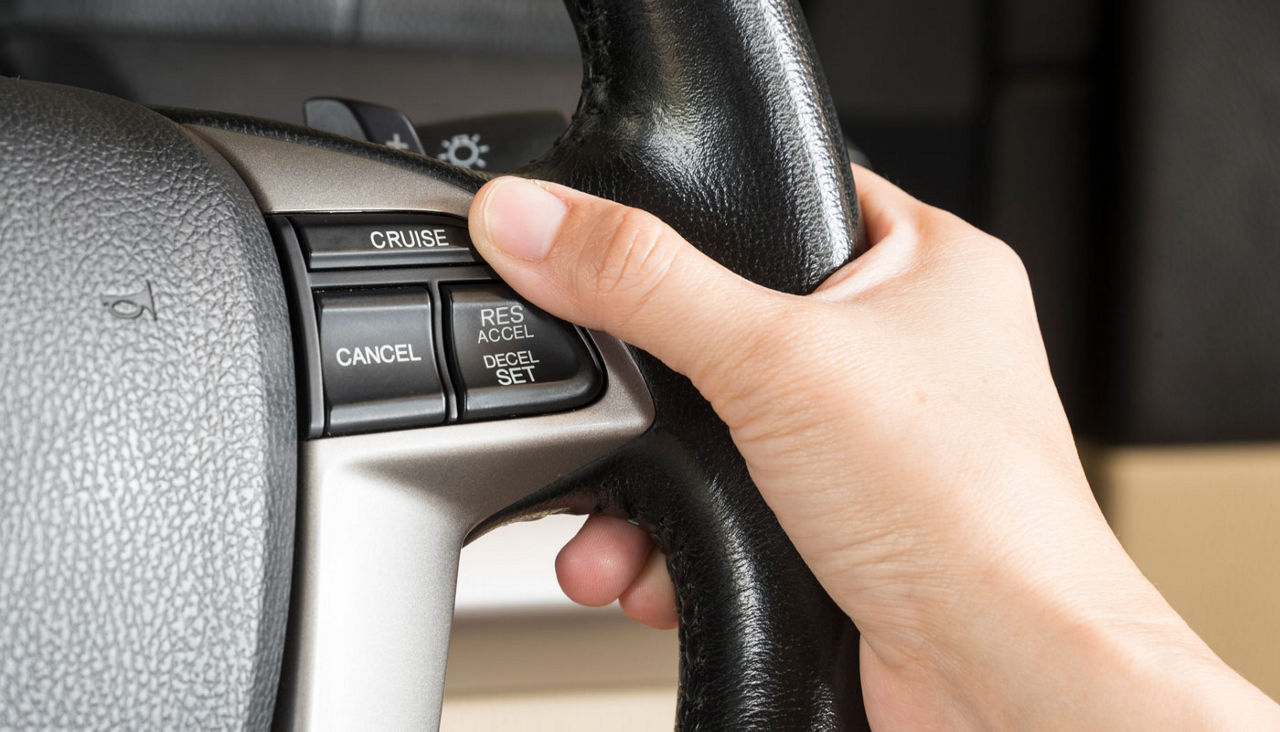 Close-up of one hand on a steering wheel next to the cruise control button.