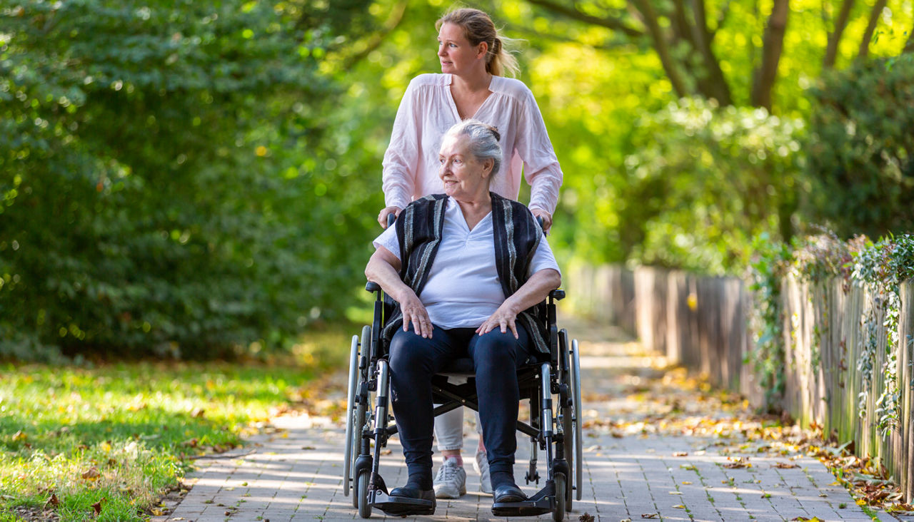 A young woman pushes an older woman in a wheelchair through a park