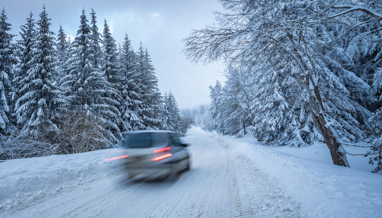 Driving a car in a remote snowy winter road through a pine forest