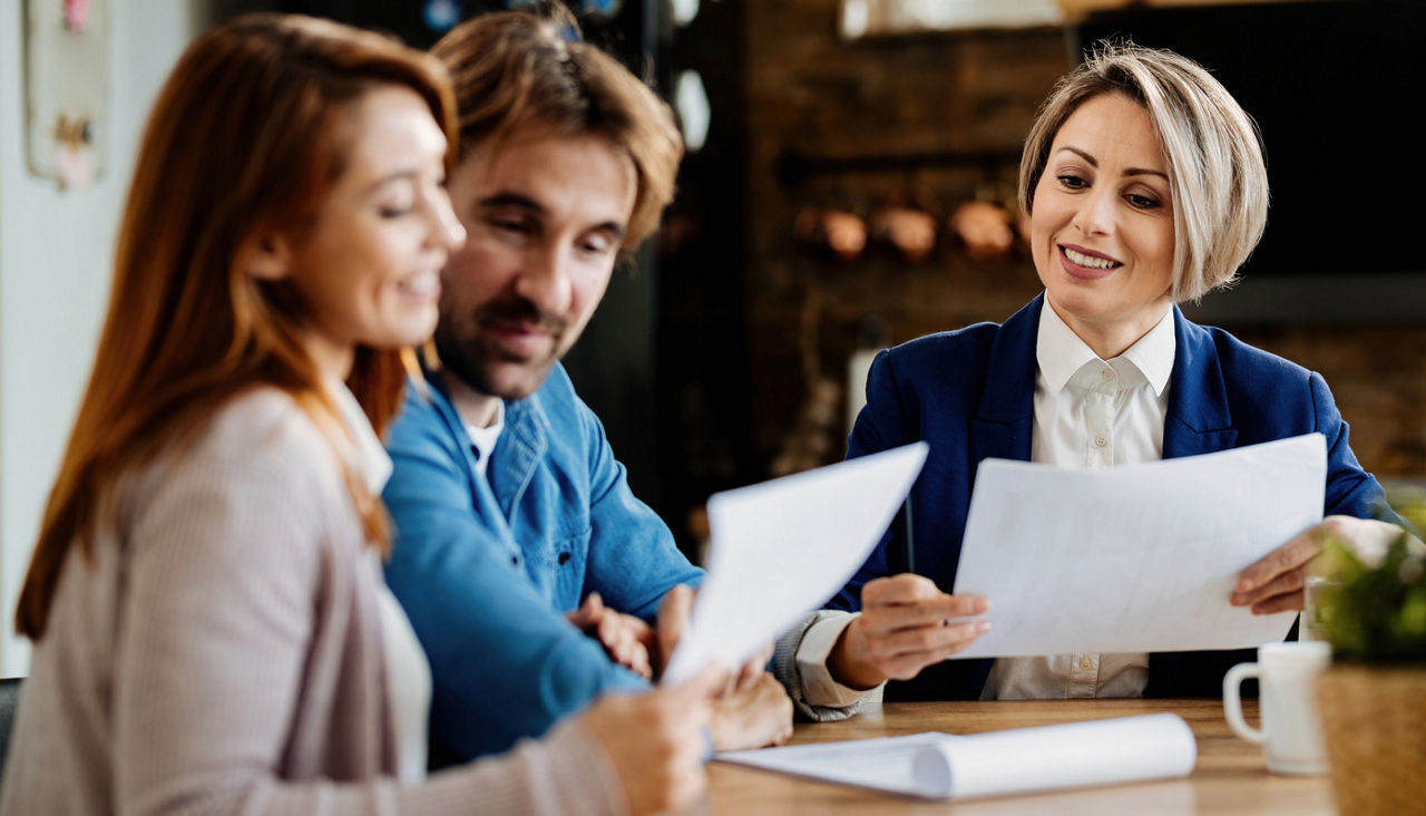 Financial advisor and young couple reviewing paperwork during a meeting at home