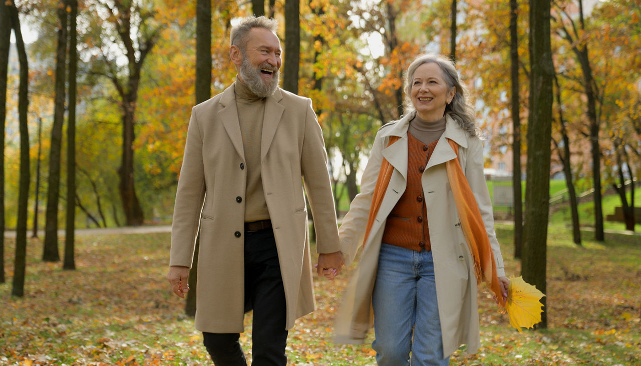 Happy senior couple holding hands together walking in park in the fall