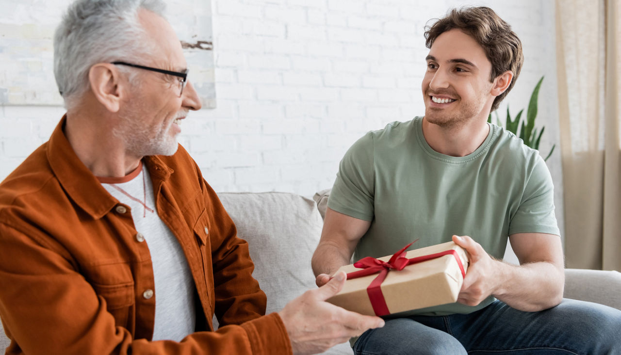Son gifting dad on Christmas and giving him gift box on couch at home