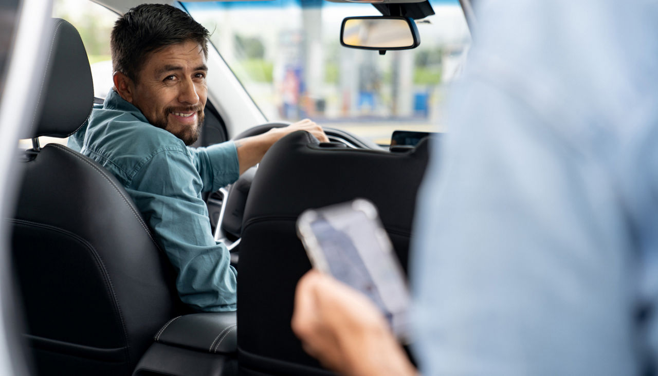 RIdeshare driver looking back at passenger holding a phone