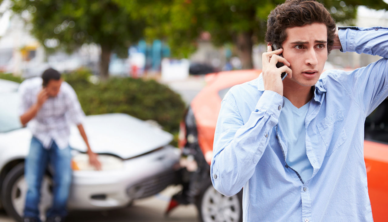 Teenage driver making phone call after car crash in front of his car and another one