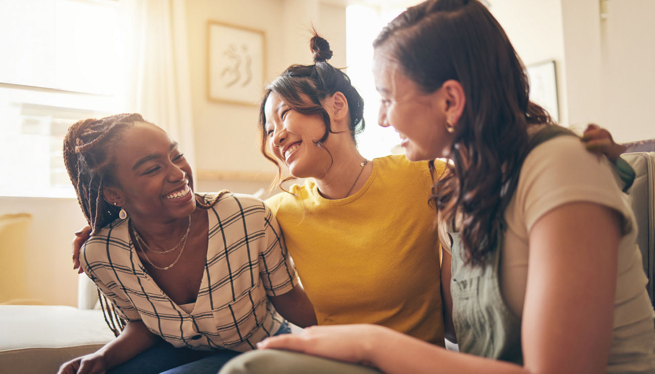 Three young women hugging and smiling and having a good time in a home 