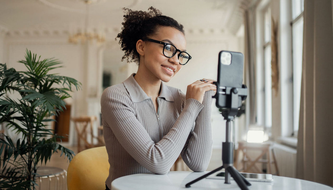 Smiling woman with glasses filming herself on her smartphone in a bright, elegant room