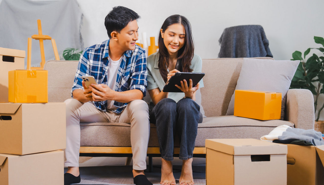 Couple is unpacking boxes in a living room and using a tablet to check items off