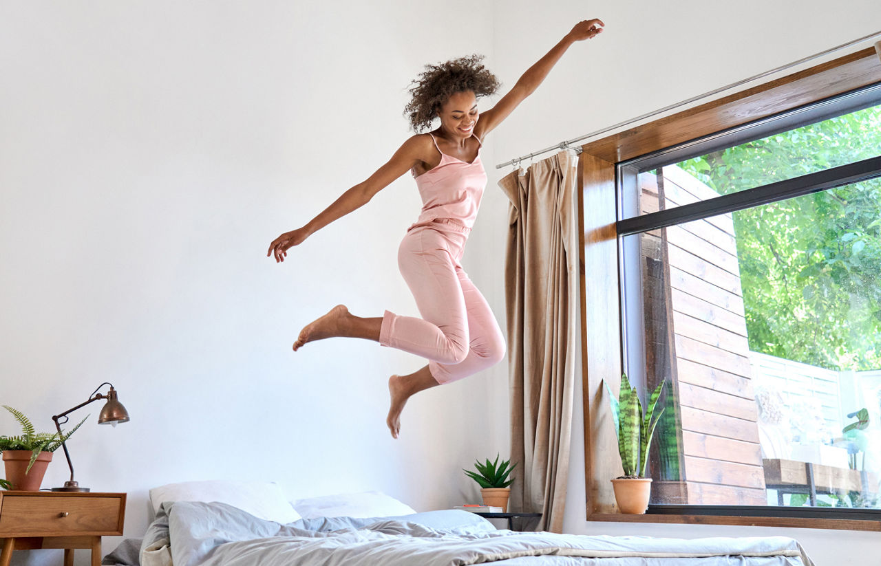 Happy young woman in pajamas jumping on bed