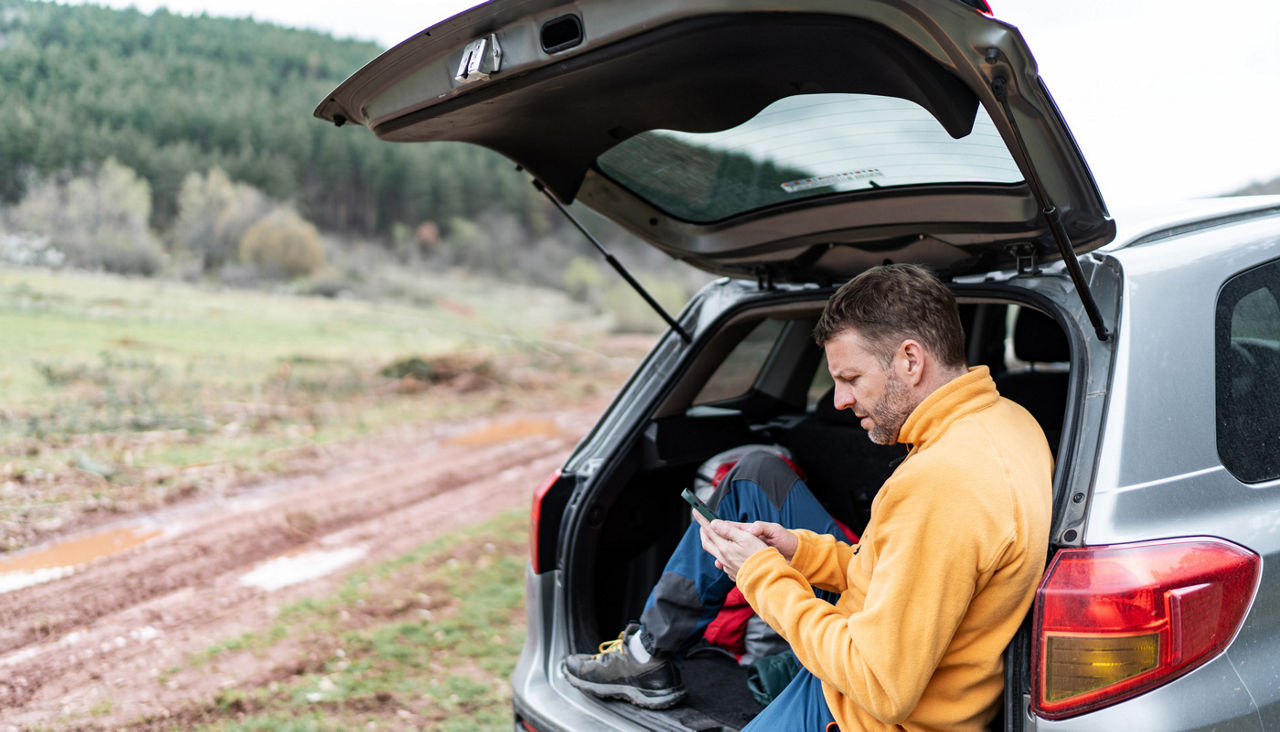 Man resting in car trunk using smartphone