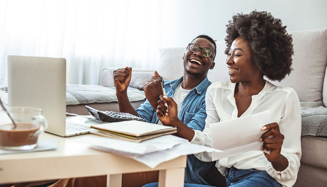 African American young man and woman smiling and cheering in front of paperwork and laptop