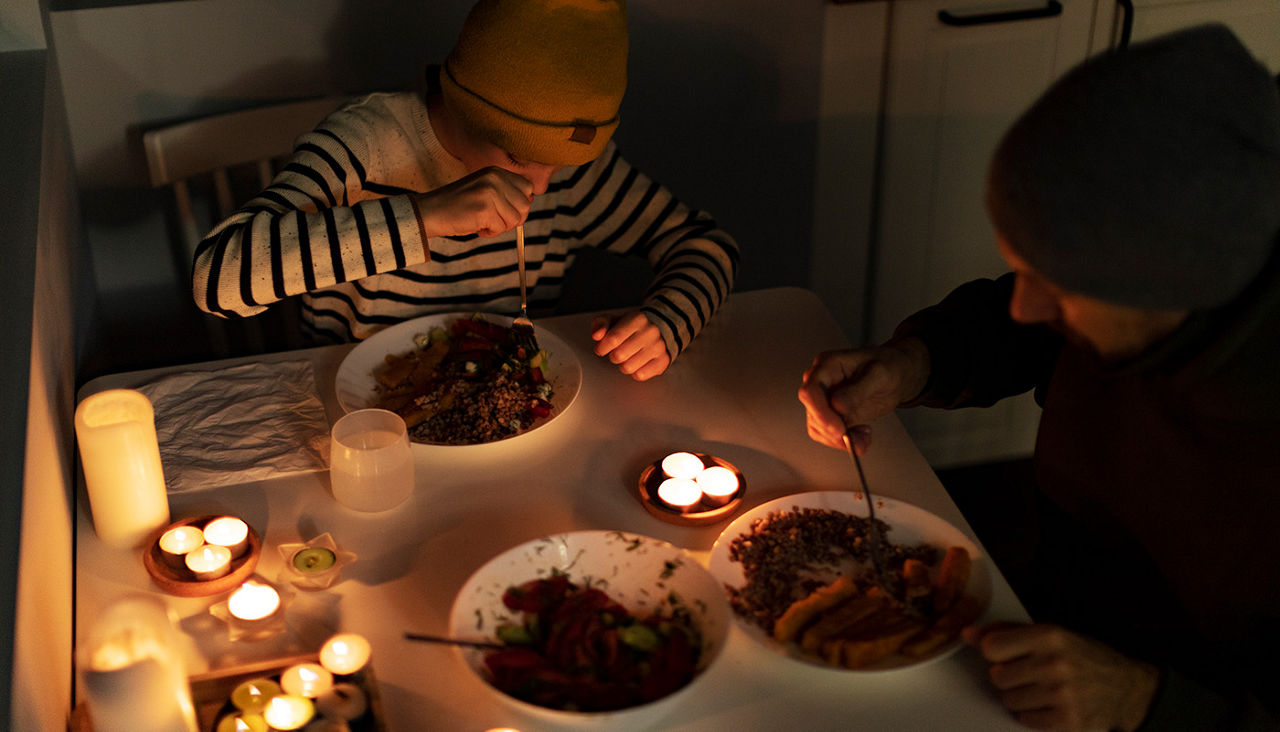 Father and son in warm clothes eating at table by candlelight