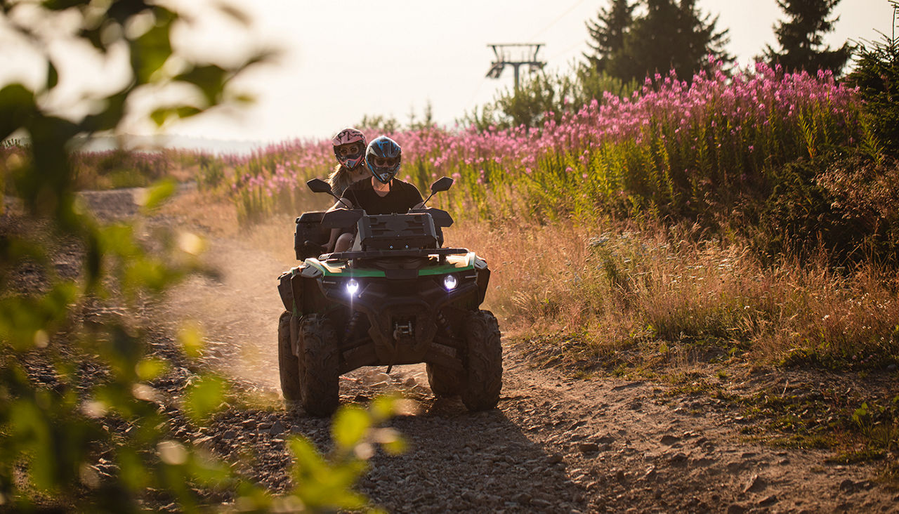 Sporty boyfriend and girlfriend on a mountain riding around on a quad bike