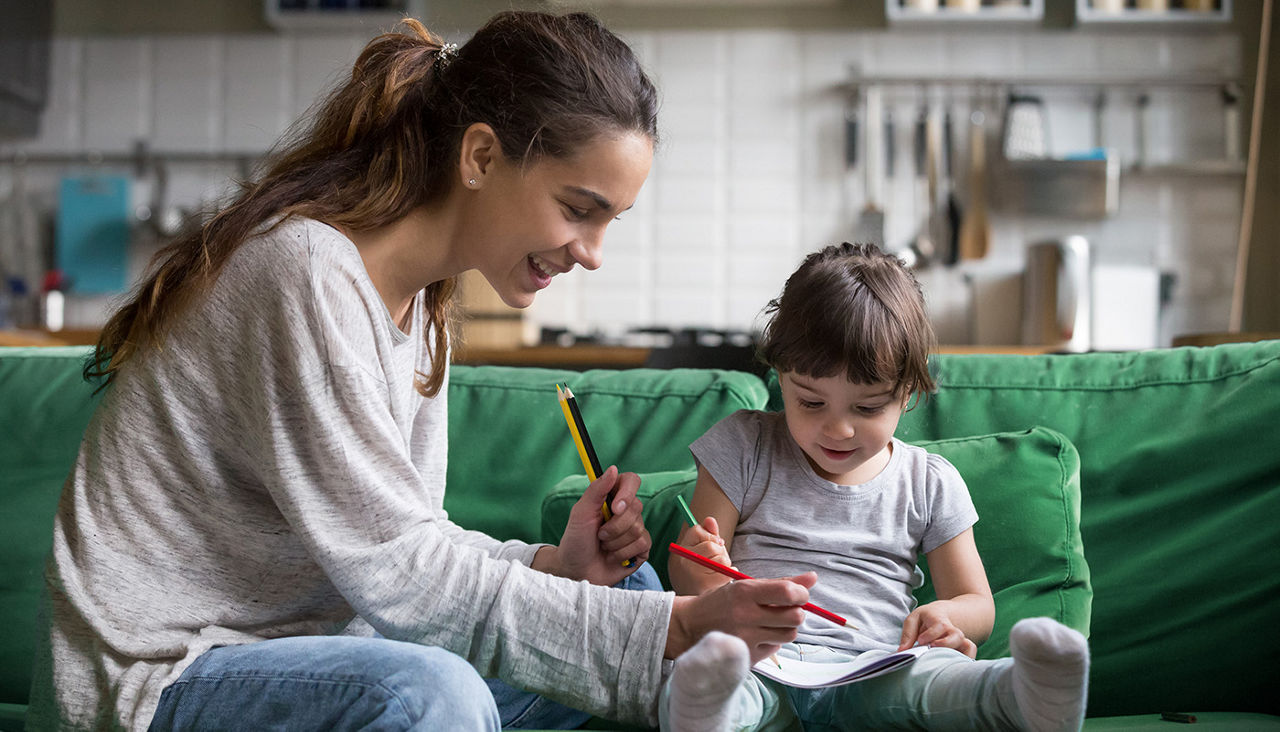 A teen girl and toddler sit on green sofa and color together