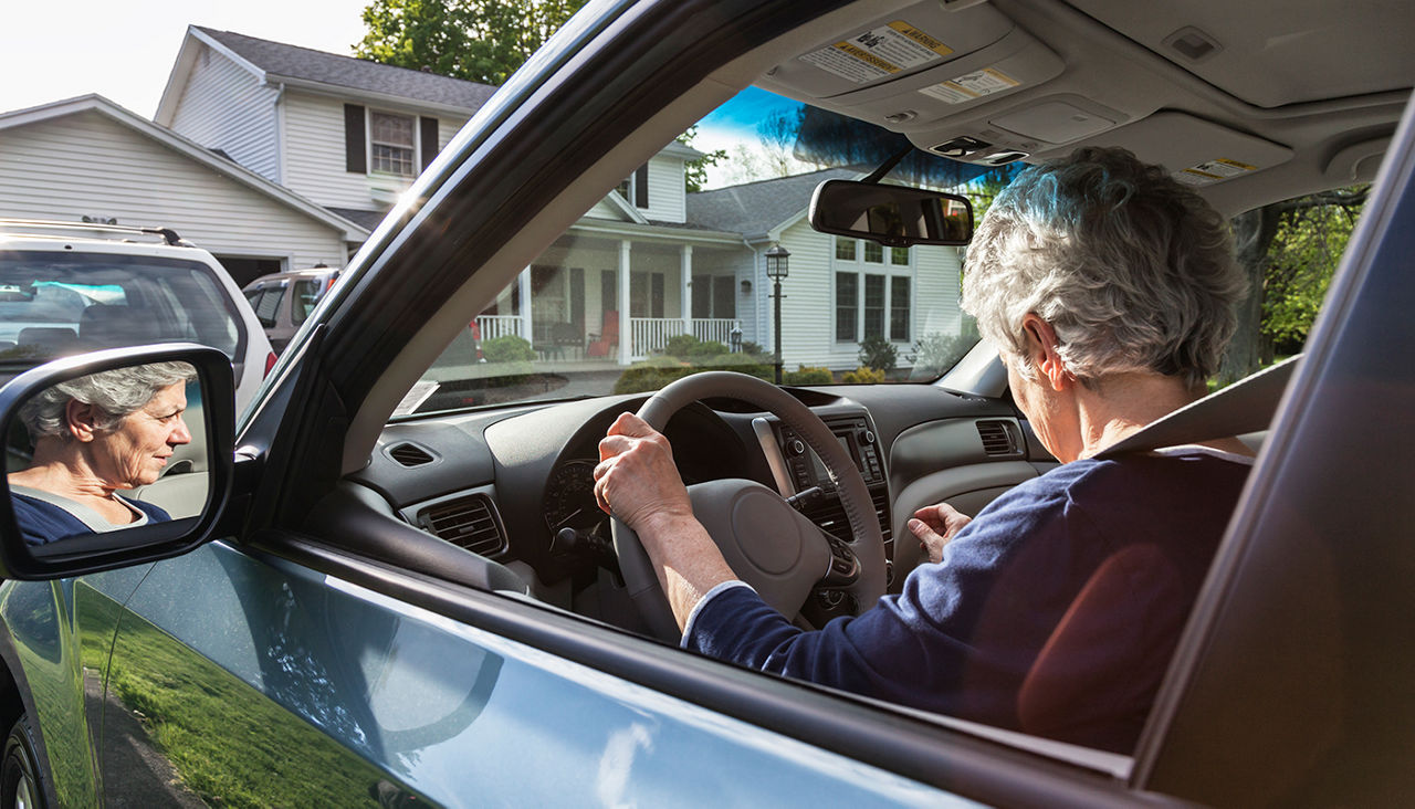 An older woman behind the wheel of a car looking confused.