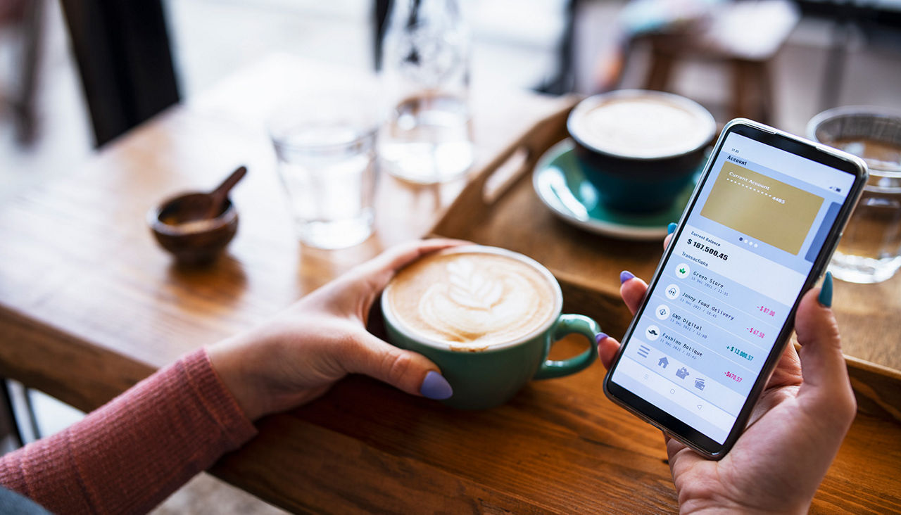 Closeup of hands holding a cappuccino and smartphone