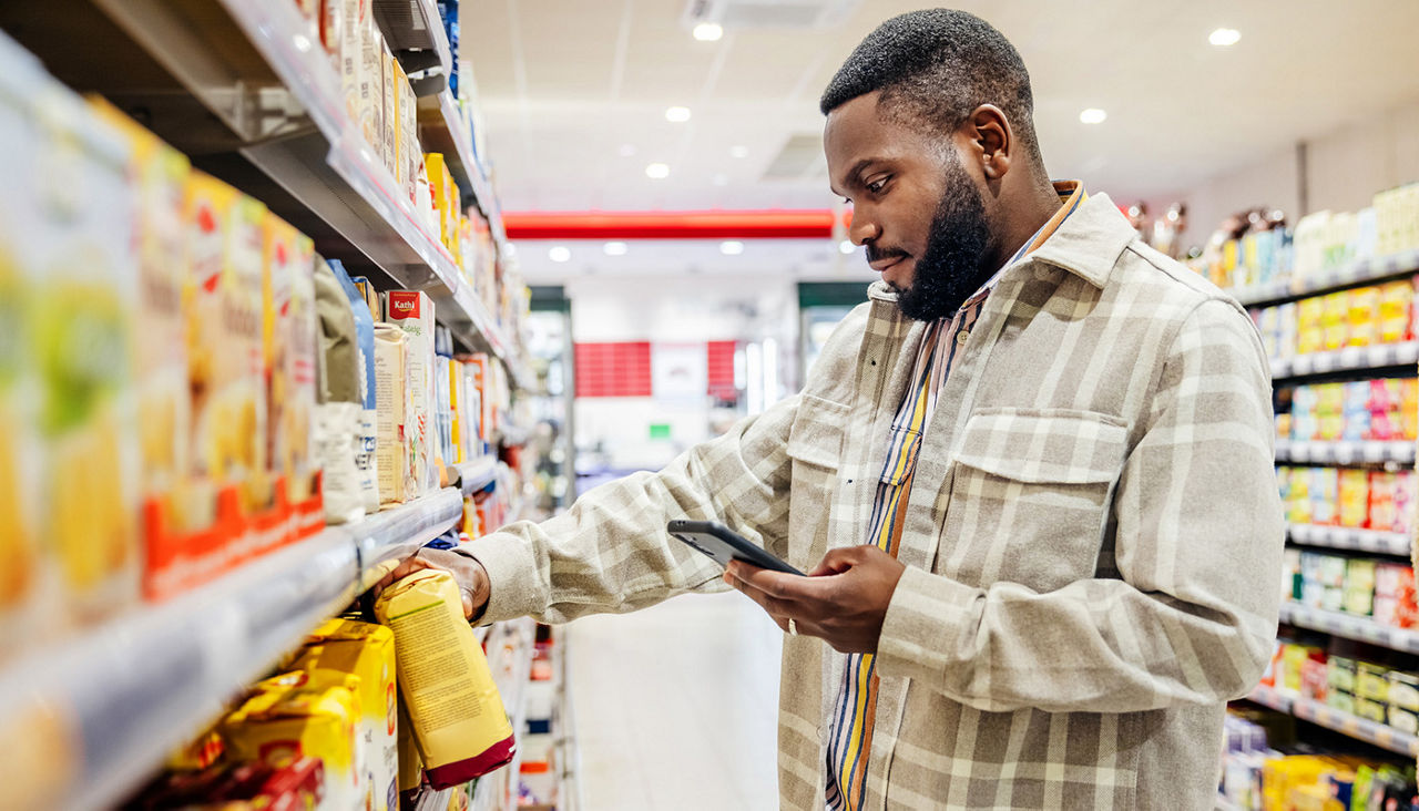 A man using his smartphone to look up ingredients and prices wile choosing items in his local supermarkets.