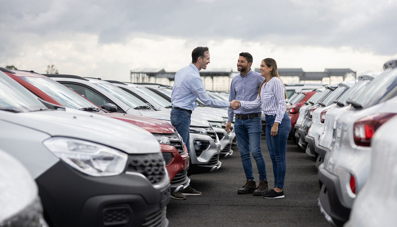 Happy couple handshaking with a car salesperson after buying a car at the dealership