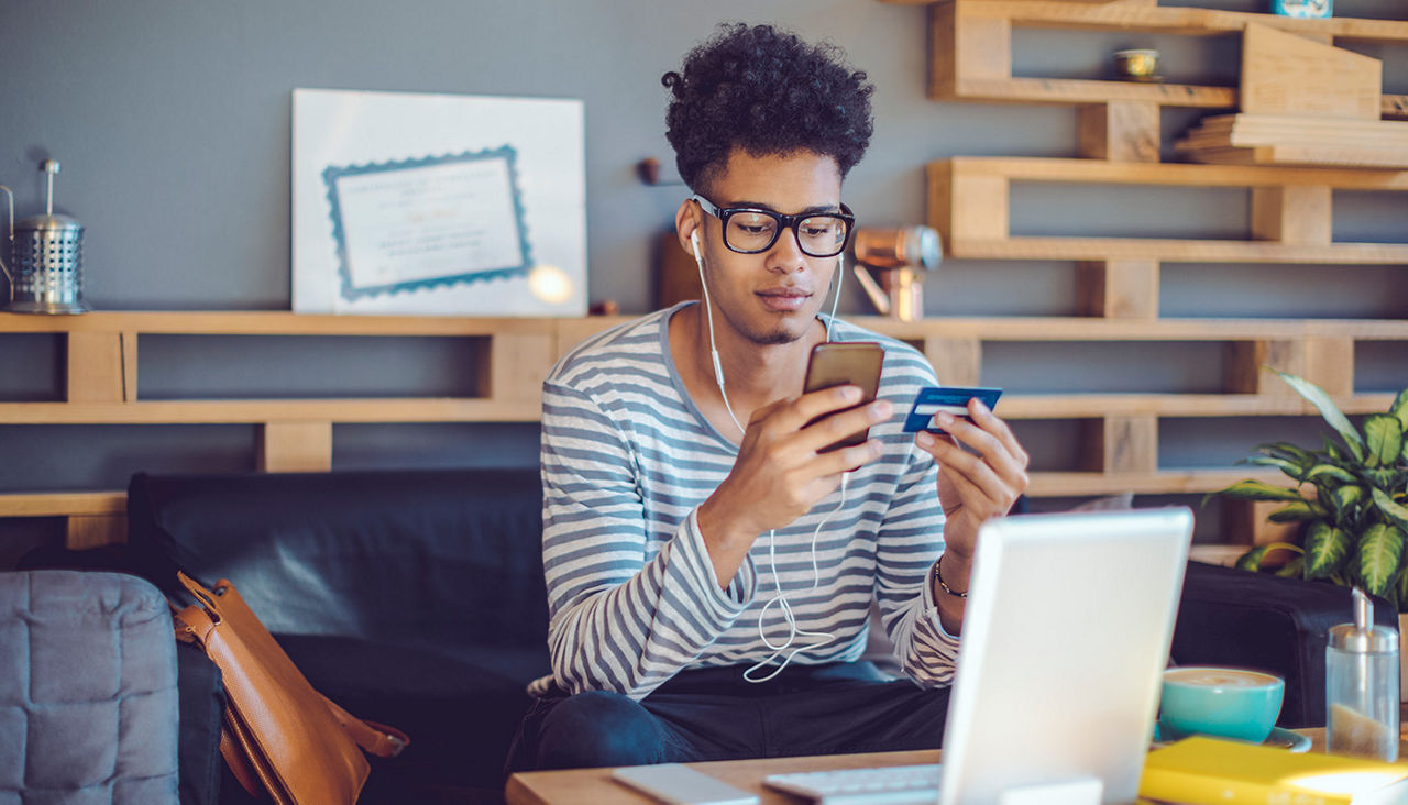 A person with earphones holding a cell phone and a credit card.