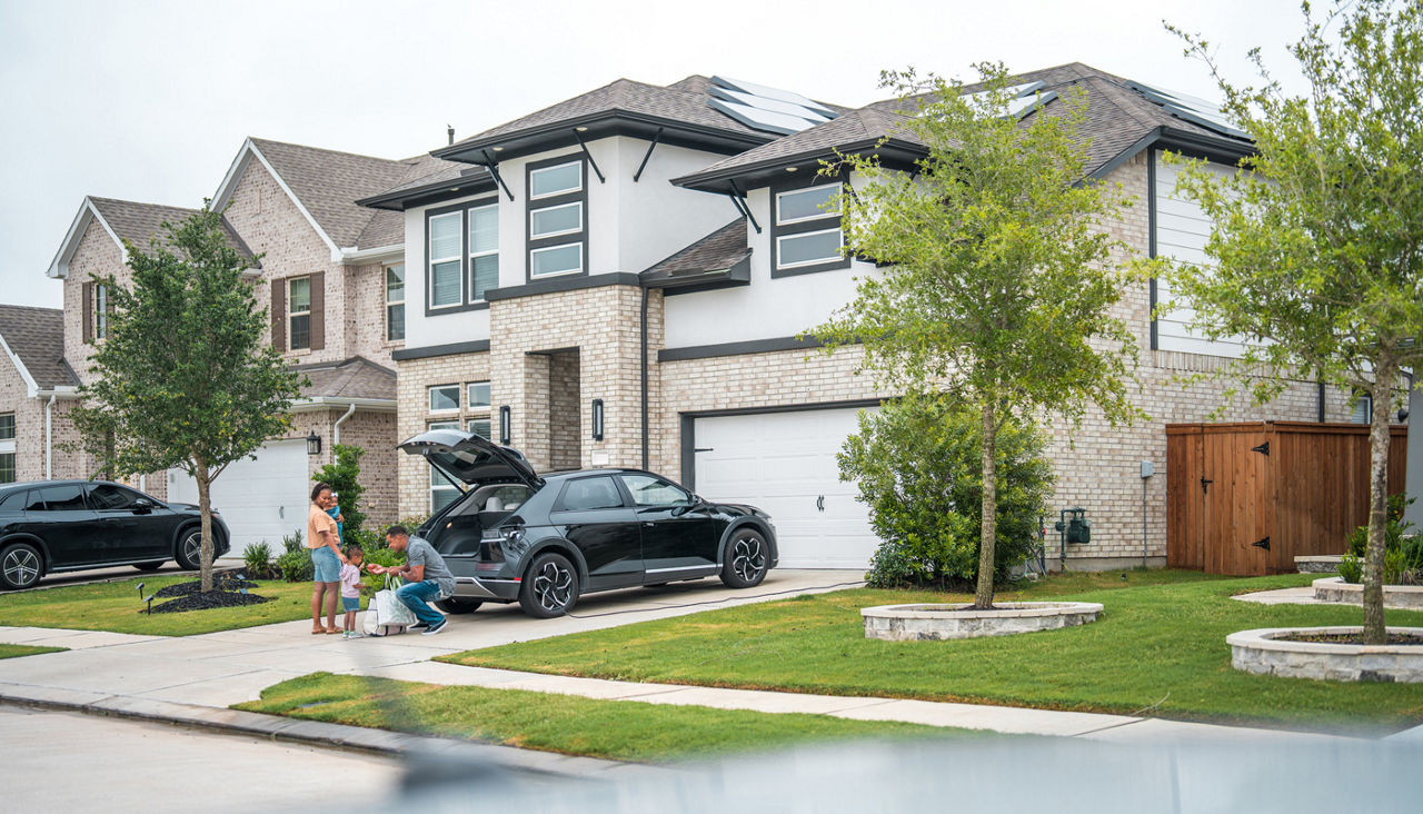 Family unloading groceries in driveway of home.