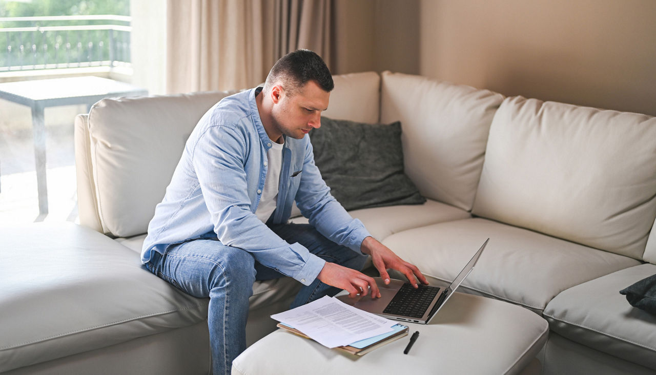 Man working with laptop and documents at home on couch
