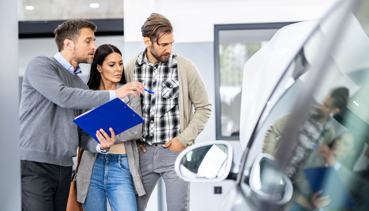 Salesman showing buying plans to young couple in auto repair shop.